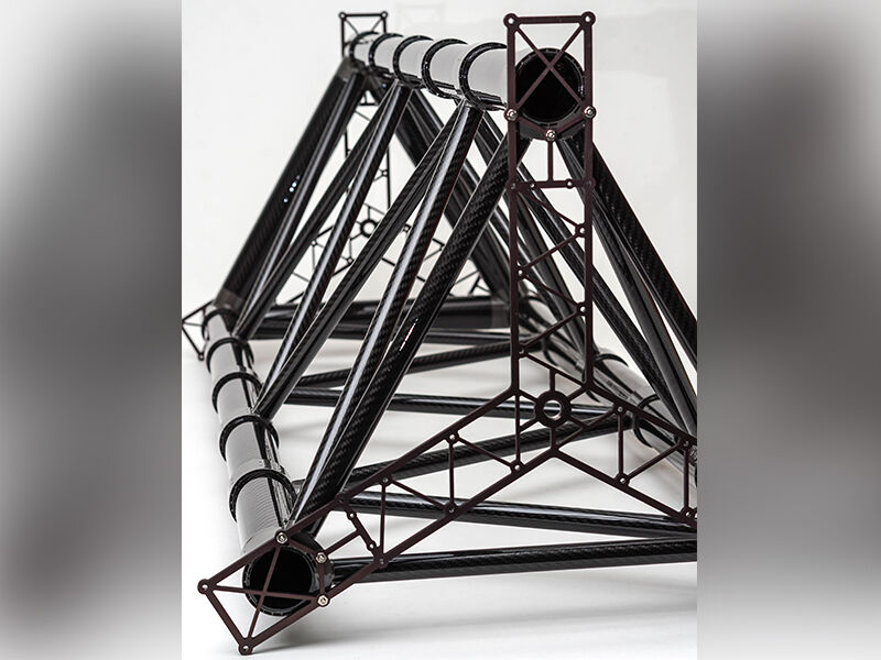 Close up image of the end of the truss structure. The primary structure is triangular in shape and laying on its side. Image looks down the entire structure. There are truss-like substrates radiating from the center of the truss and that are attached to the three primary posts. The structure is on a white background.